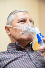 Senior man using medical equipment for inhalation with respiratory mask, nebulizer