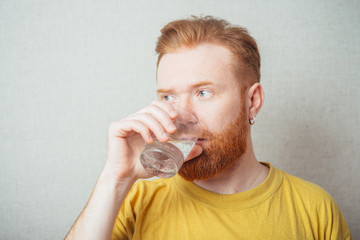 on a gray background man with a beard in a yellow T-shirt drinks water from a glass