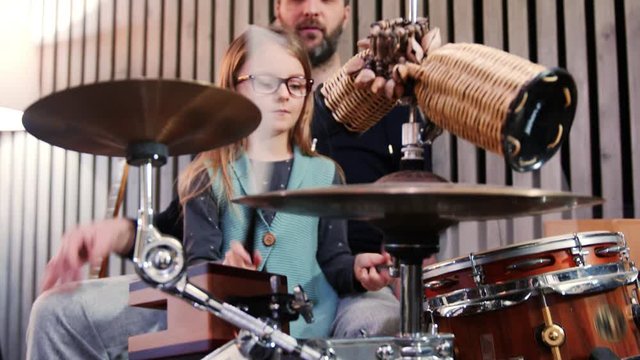 Father and daughter play percussion together.Little girl learning drums with her dad at home.Front view.Percussion class at home