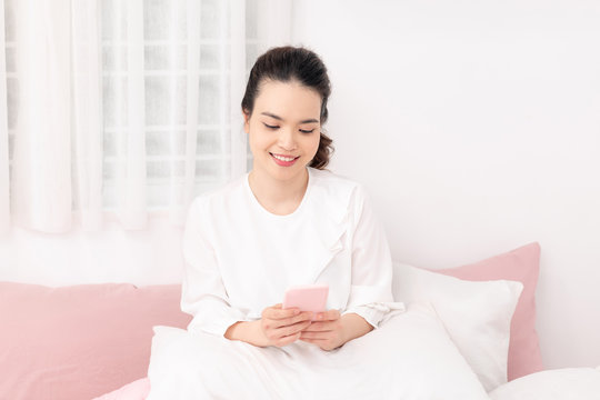Cheerful teengaer uses mobile phone for online chatting, networking, recieves text message in bed