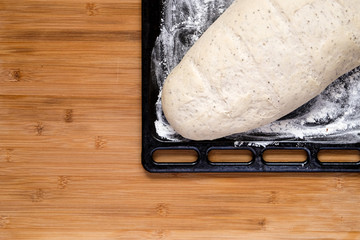 Raw dough for bread ready to bake on a black baking tin and a wooden board.