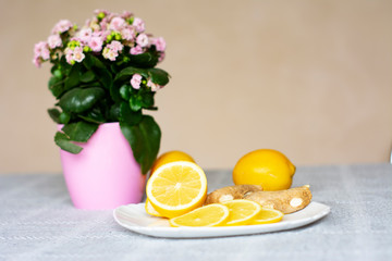 On the table in a plate are ginger and lemon. Near the Kalanchoe flower.
