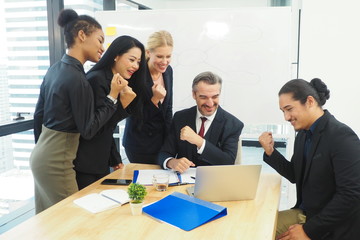 Group of multinational people working together in the office looking at their laptop after getting work done successfully. All smiling and feeling excited with lifestyle and happy workplace concept