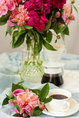 Obraz na płótnie Canvas Spring or summer still life with beautiful flowers, drinks and light cloth on the table. Lush bouquet of pink and red peonies, pourover for making filter coffee and cup of hot espresso