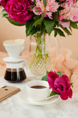 Fototapeta na wymiar Beautiful spring or summer still life with beautiful flowers, drinks and light cloth on the table. Lush bouquet of pink and red peonies, phone,pourover for making filter coffee and cup of hot espresso