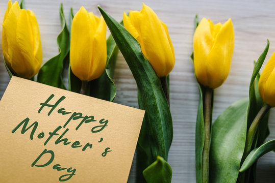 Happy mother's day. Text sign on craft postcard on yellow tulips background. Greeting card concept. Sensual tender women image. Holiday greeting card for Mother's Day! Top view, flat lay.