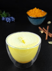 Golden milk with turmeric and other spices on a black background. Traditional drink to support immunity against flu and the common cold. Close-up, spices and ingredients for a drink at the table.