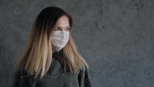 young woman puts on protective medical mask on her face against gray wall