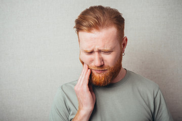 a young man with a beard in shirt feels toothache