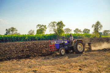 Obraz premium Indian / Asian farmer with tractor preparing land for sowing with cultivator, An Indian farming scene.
