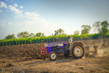 Indian / Asian farmer with tractor preparing land for sowing with cultivator, An Indian farming...