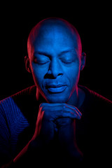 Black man with blue and red light, eyes closed, isolated on black background. Meditation concept.