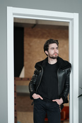 A young stylish man with a beard and dark hair in a black leather jacket with faux fur collar 