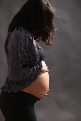 A pregnant woman with a bare stomach is wearing a black background with a brown background