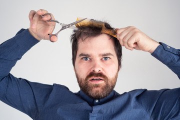 Obraz premium man with a comb and scissors in his hands cuts his hair