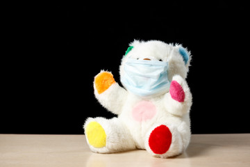 A soft toy bear in a protective medical mask, sits on a dark background. Concept of quarantine of schools, home education. Copy space