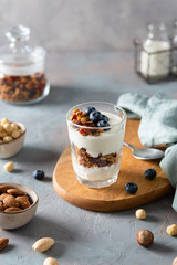 Crunchy honey granola with yogurt in a glass on gray background. Dry breakfast cereals with flax seeds, cranberries and nuts. Healthy, vegeterian fiber food. Breakfast time. Dieting concept. Side view