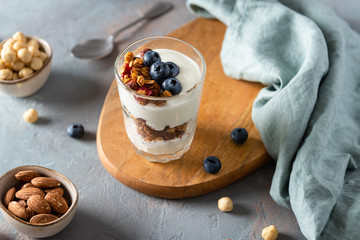 Healthy Breakfast. Muesli with blueberries, almonds, raisins, hazelnuts, honey and yogurt in a glass on a dark concrete background. Side view