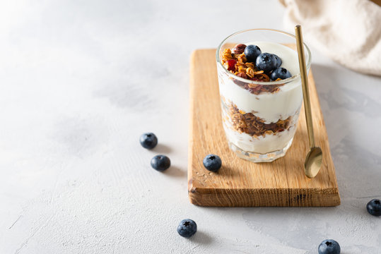 Healthy blueberry parfait in a glass on a wooden board on white background. Side view, copy space. Healthy nutrition recipe