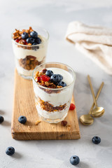 Homemade granola with honey, oatmeal, cashew nut, almond, hazelnut, walnut, raisin and cranberry in glassesl with yogurt on light concrete background, side view