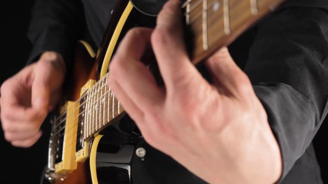 Guitarist plays a light brown six-string electric guitar with a pick against black background. Concept of stay home and make some music. Free time for sound art. Close up. 4K