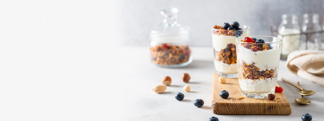 Granola, cereal breakfast banner. Blueberry parfait in glasses on wooden board on gray background....