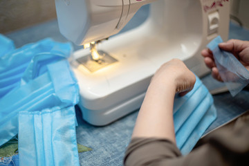 Sewing Homemade protective medical mask in process. woman holds a spunbond, sms, Meltblown mask at home. Detail White modern sewing machine and three-layer masks.
