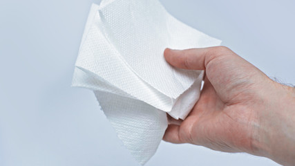 The male hand holds an unwound piece of toilet paper in his hand to protect against coronavirus during quarantine. Isolated on a gray background in the studio. Coronavirus concept