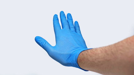 Male hand in a blue medical glove stops the coronavirus in front of him. Isolated on a gray background in the studio. Coronavirus concept. Stay at home. Quarantine.