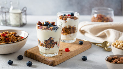 Morning granola breakfast with raisins, cranberries and hazelnuts served with yogurt in glasses on a gray concrete background. Side view, close up. Menu, recipe
