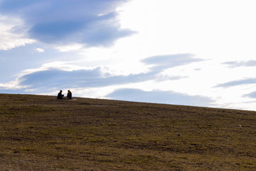 a man and a woman on a hill on a warm spring day behind them against the sky with blue clouds