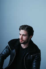 A large portrait of a stylish young man with a beard and dark hair in a black leather jacket