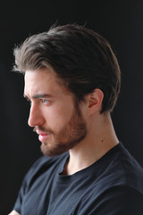 Close-up portrait of a young stylish man with a beard and dark hair in a black T-shirt 