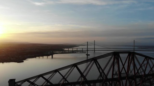Edinburgh's Forth rail bridge from a height, ariel footage revealing the beauty of golden hour and the incredible scale and engineering of all 3 bridges together.