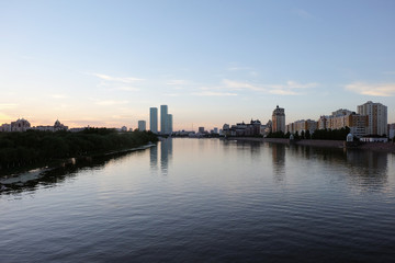 Fototapeta premium NUR-SULTAN, ASTANA, KAZAKHSTAN - JUNE 3, 2015: A beautifula panorama of Ishim river with smooth surface of water and evening city view