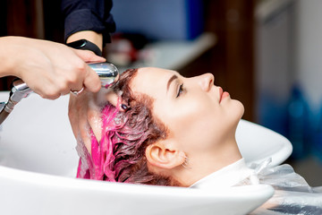 Hairdresser hands washing pink dyed hair of woman in sink, close up.