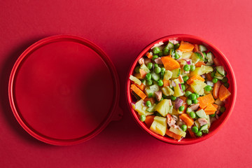 Russian vegetarian оlivier salad on the red background. Plastic lunch box