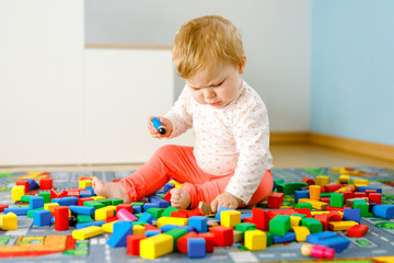 Adorable baby girl playing with educational toys . Happy healthy child having fun with colorful different wooden blocks at home in domestic room. Baby learning colors and forms