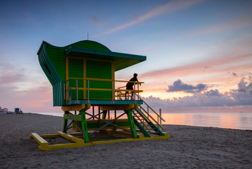 Young man on lifeguard cabin at sunrise, Miami beach, USA