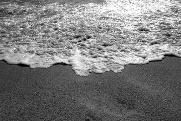 Sea wave and sandy beach in black and white.