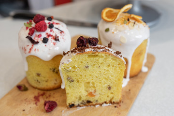 Various Easter cakes with white icing, decorated with berries and orange stand on a wooden board. Easter cutaway