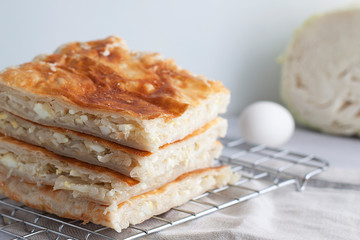 Delicious homemade puff pastry pie with cabbage and chicken egg filling. grilled pie Slices, half a head of cabbage and an egg in the background. On a white table