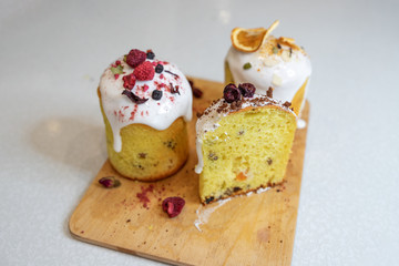 Various Easter cakes with white icing, decorated with berries and orange stand on a wooden board. Easter cutaway
