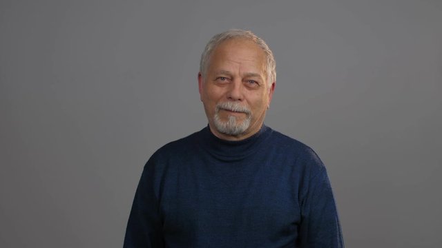 aged man with grey beard and hair nods head with enigmatic smile looking into camera close view. Concept man emotion
