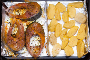 Raw steakes of white fish silver carp, potatoes, spices in a cooking tray or deco.