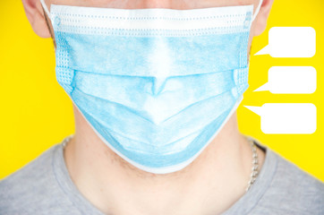 A man in a blue medical mask looks at the camera, sideways. Coughs through the mask into a fist, hand. A man in a gray T-shirt on a yellow background. Place for text. COVID-19