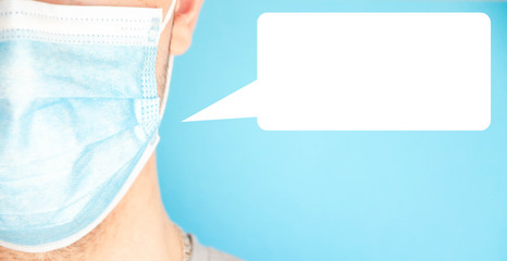 A man in a blue medical mask looks at the camera, sideways. A man in a gray T-shirt on a blue background. Place for text.  Copy Space. Covid-19
