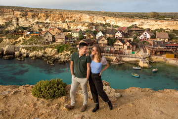 Happy beautiful traveller couple posing on rocks near village
