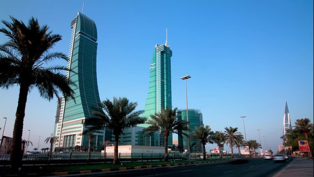 Timelapse of the King Faisal Highway in Manama with cars speeding in the foreground and the iconic Bahrain Financial Harbour twin towers in view with palm trees in the median.