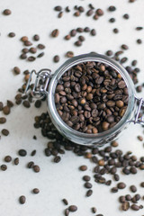 Macro shot of a transparent jar filled with coffee beans in the center of the photo and coffee beans around the jar